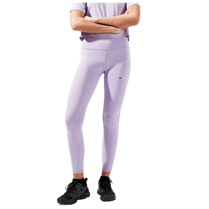 A person is standing with crossed arms wearing light purple leggings and a matching top paired with dark athletic shoes in a neutral background environment.