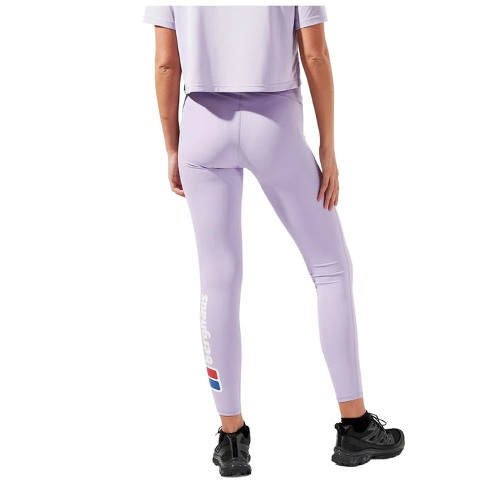 A person is standing with their back facing the viewer wearing lavender leggings and a cropped top with black shoes in a neutral setting. The leggings have a logo on the side.